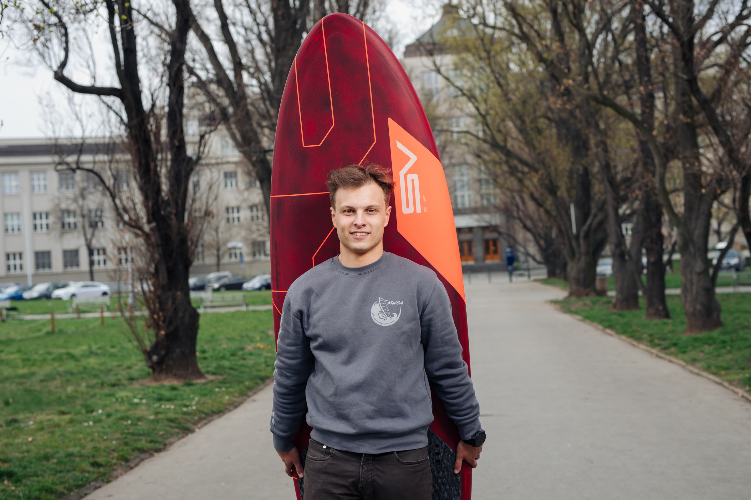 Matěj Červenka standing outdoors with a red windsurf board
